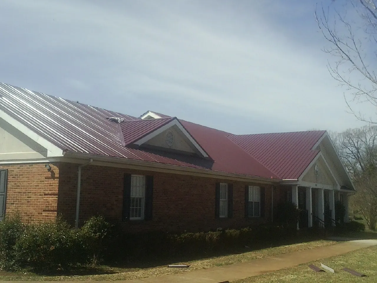 Red metal roof with gabled entries on a long brick building, from a Hail Damage Roof Repair job in Wenham