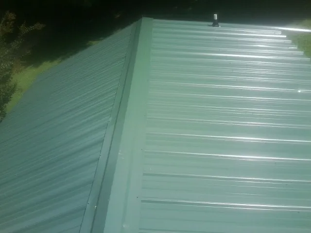 New green metal panels meeting at the ridge of a roof — Flat Roof Repair work by our crew in Wenham