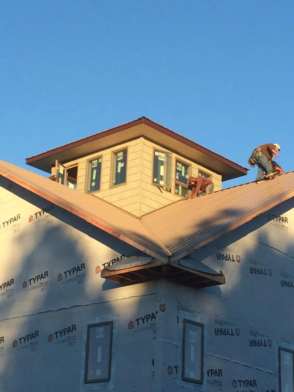 Roofers working around a rooftop cupola on a new metal roof at sunset — Roof Waterproofing in Wenham by Roofing Brothers